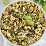 Mexican Street Corn Pasta Salad in white bowl with lime slices and chopped cilantro