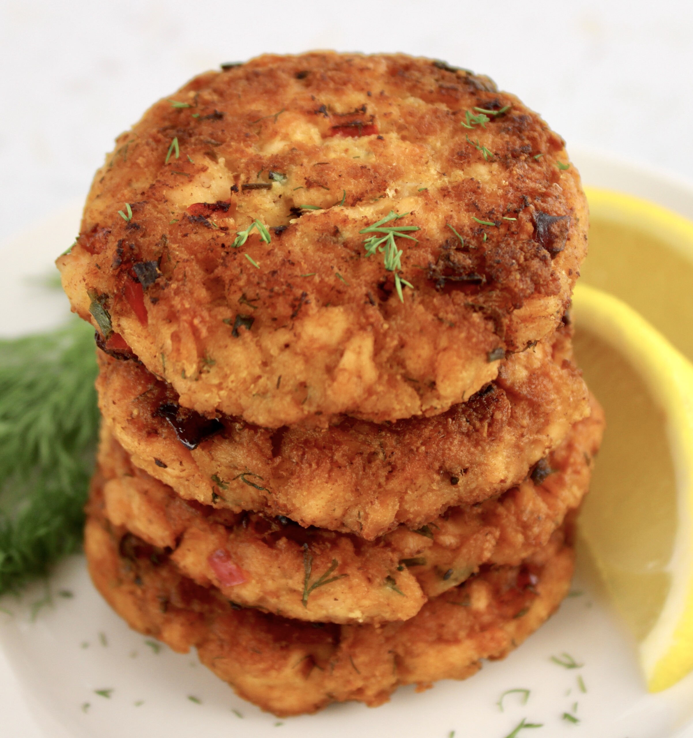 stack of Salmon Patties on white plate with lemon and fresh dill on side