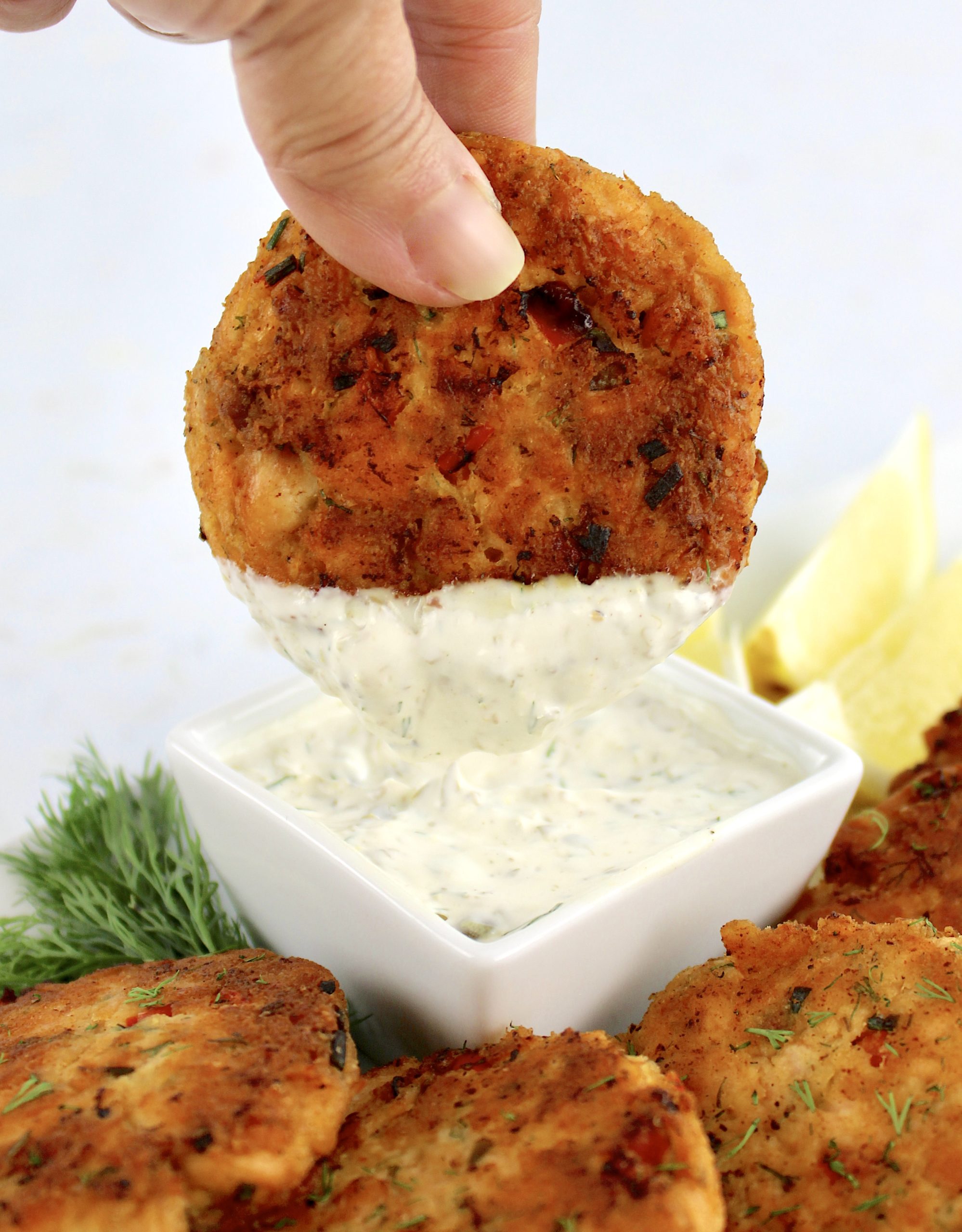 salmon patty being dipped into dill sauce in white cup