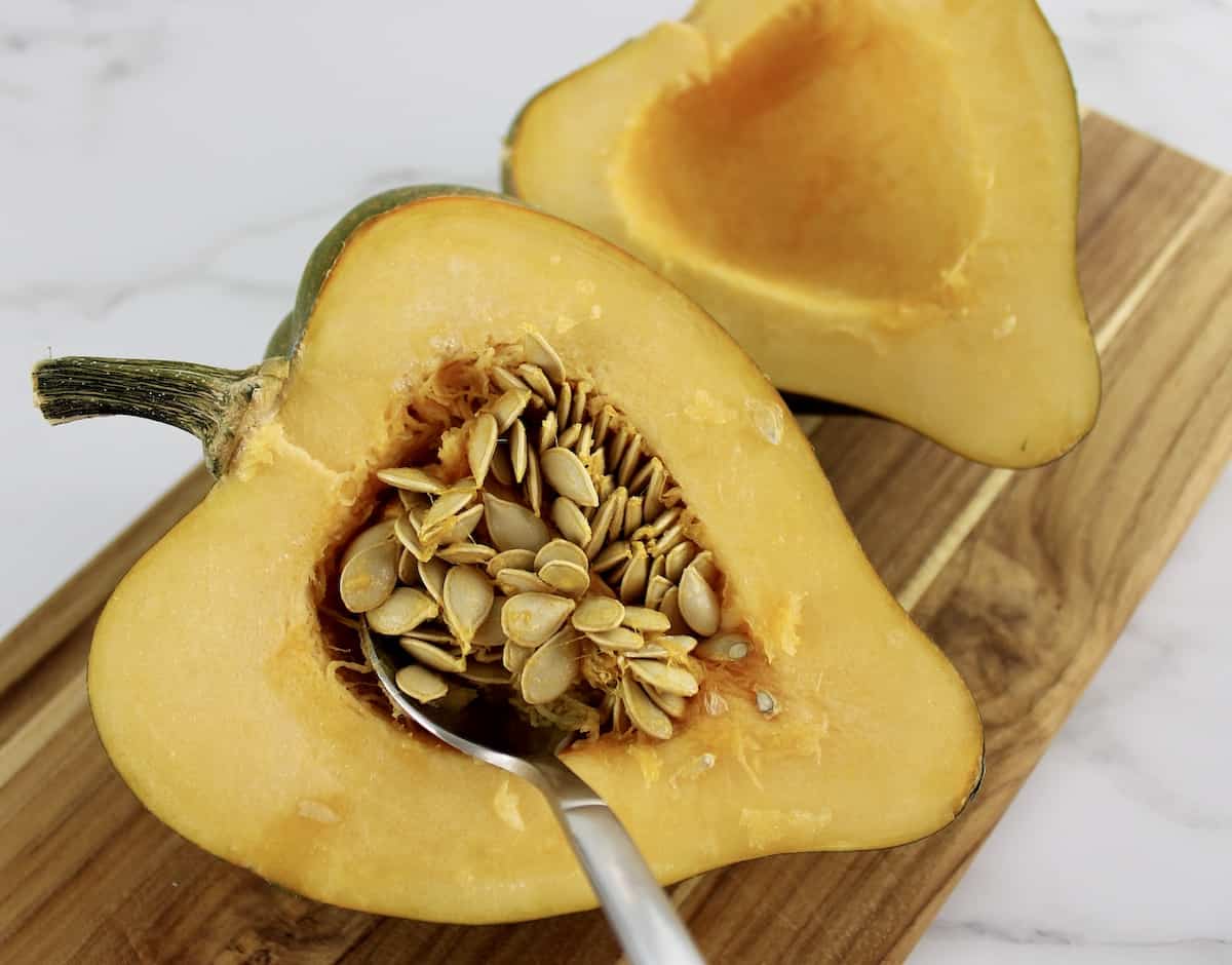 acorn squash cut in half on cutting board with seeds being scooped out