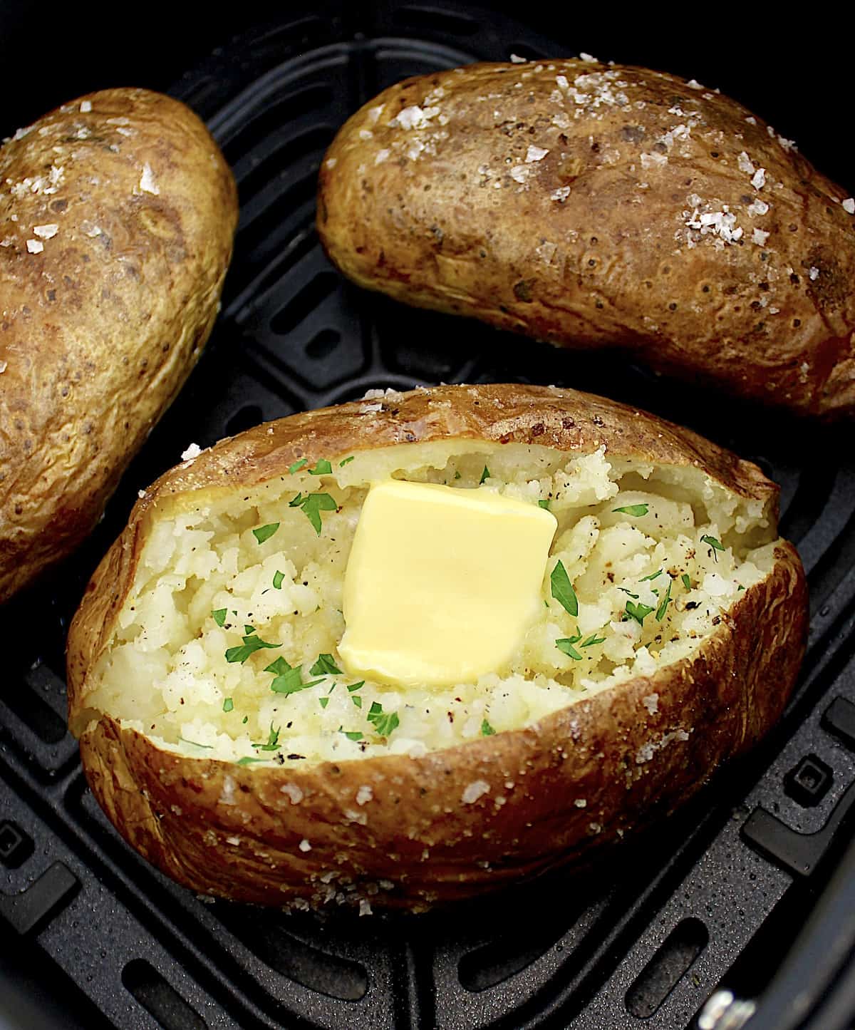 closeup of air fryer baked potato with pat of butter and chopped parsley