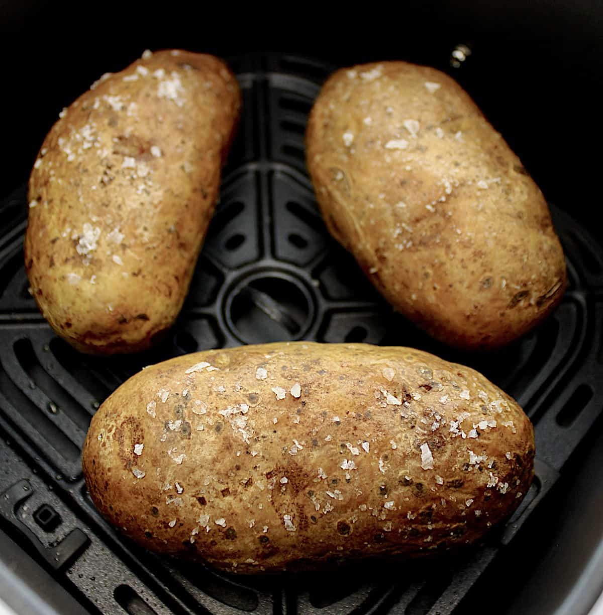 3 baked potatoes with salt on the outsides in air fryer basket
