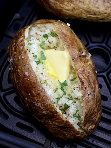 closeup of air fryer baked potato with pat of butter and chopped parsley