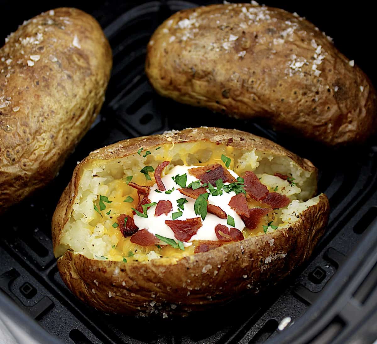 loaded baked potato in air fryer basket with 3 baked potatoes
