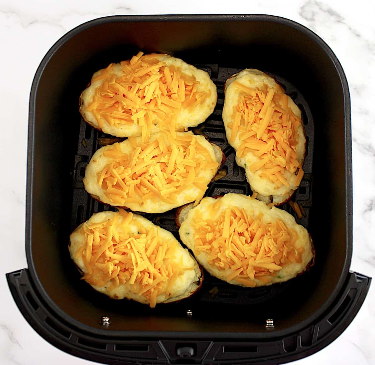 5 Air Fryer Twice Baked Potatoes in air fryer basket with cheddar cheese on top