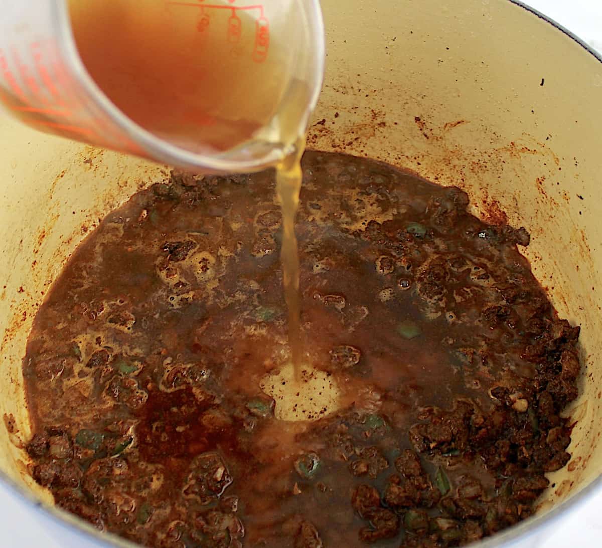 broth being poured into pot with spices, onions and peppers