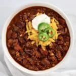 Best Homemade Chili in white bowl with shredded cheese, sour cream and sliced jalapeno on top