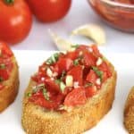 slice of Easy Bruschetta with tomatoes and garlic in background