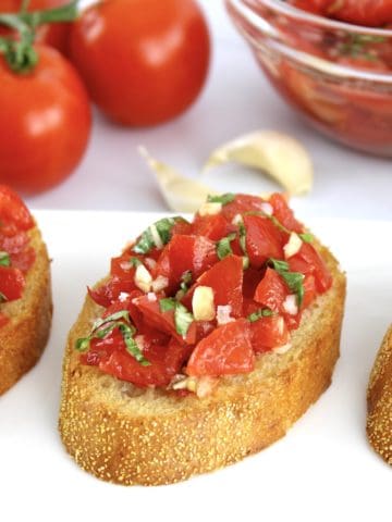 slice of Easy Bruschetta with tomatoes and garlic in background