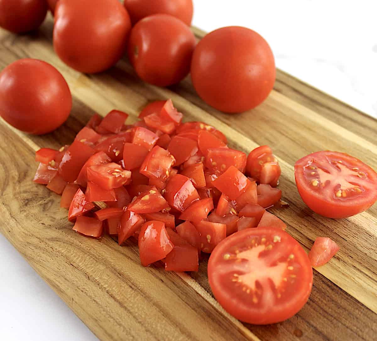 diced tomatoes on cutting board with whole tomatoes in background