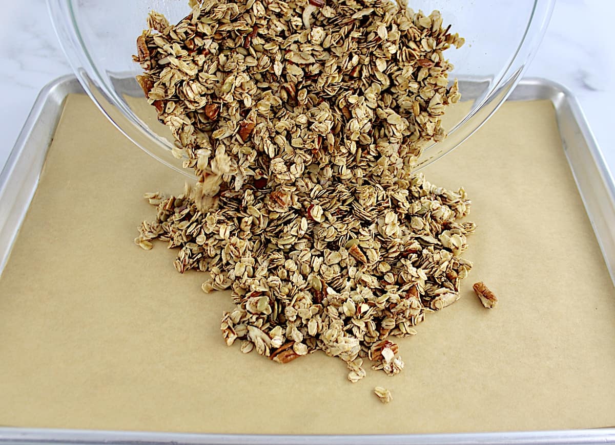 uncooked granola being poured onto parchment lined baking sheet