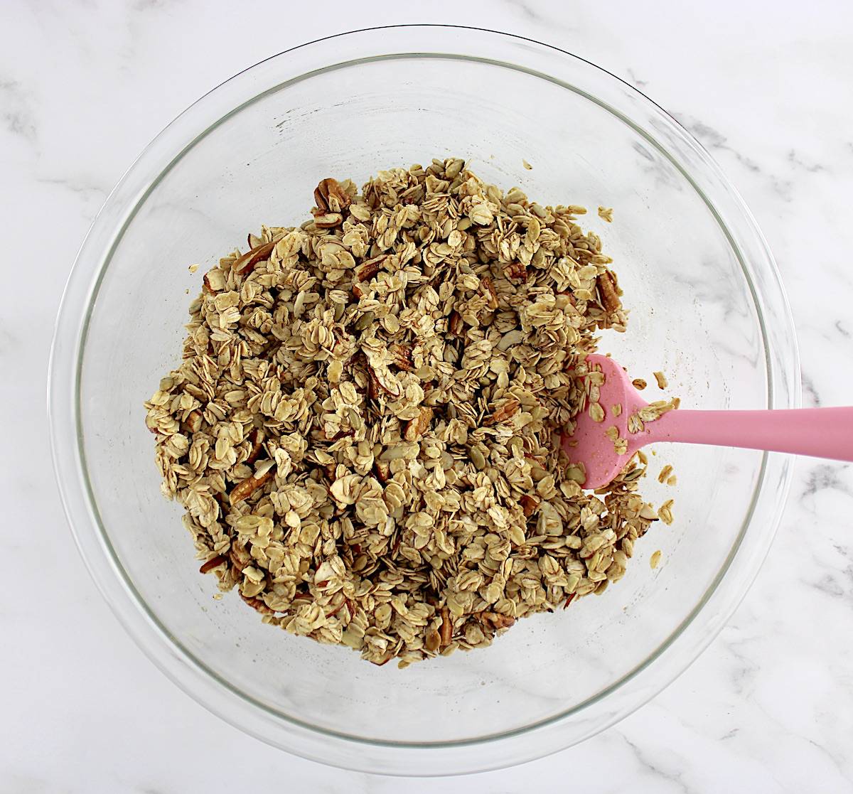 Homemade Granola unbaked in glass bowl being mixed with pink spatula