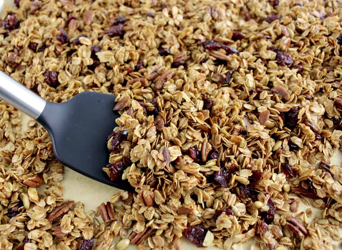 Homemade Granola on baking sheet being mixed with black spatula