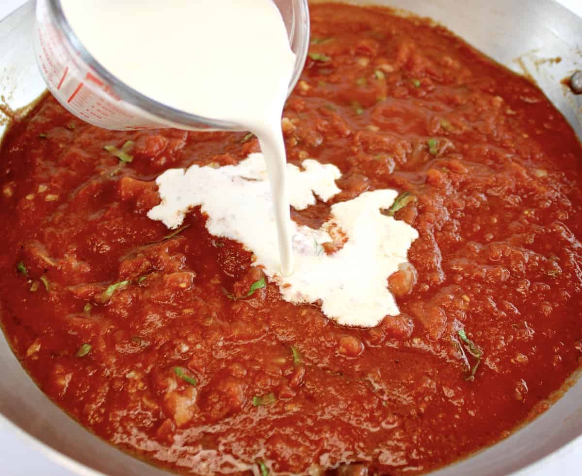 heavy cream being poured into tomato sauce in skillet