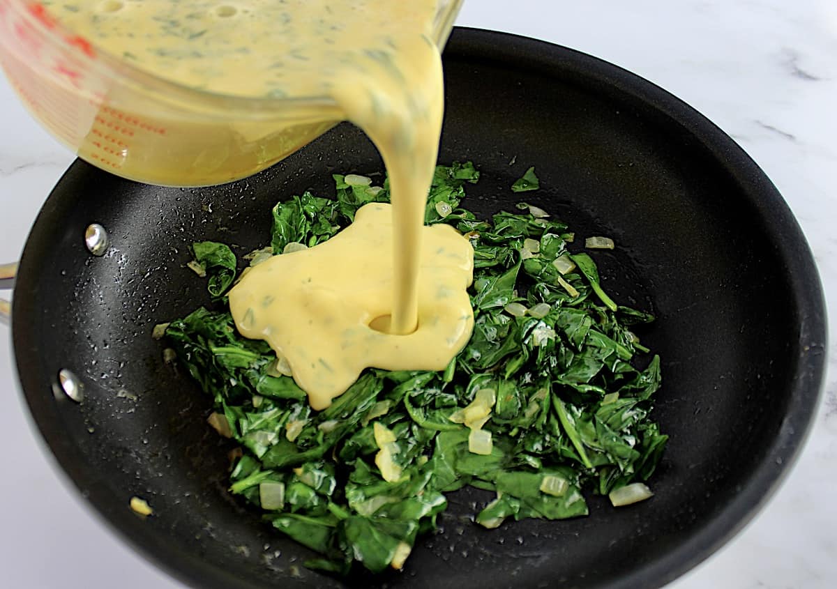 egg mixture being poured into skillet with cooked spinach and onions