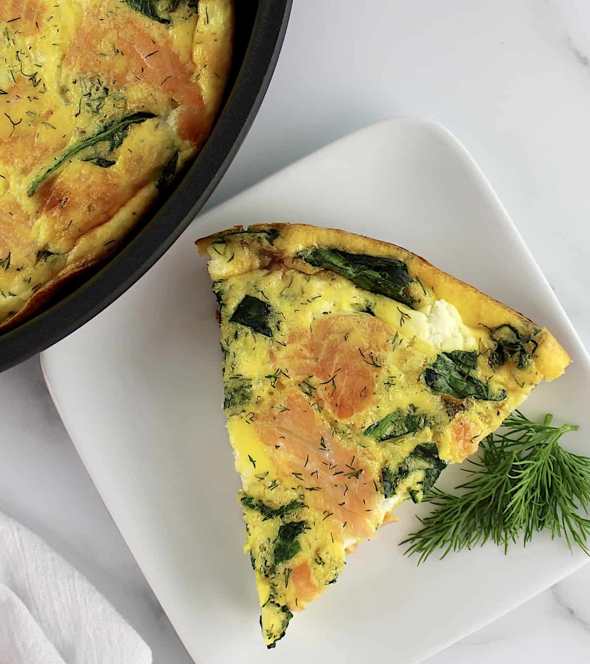Smoked Salmon Frittata slice on plate with sprig of dill and skillet on side