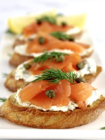 4 pieces of Smoked Salmon and Goat Cheese Crostini on white plate in a row