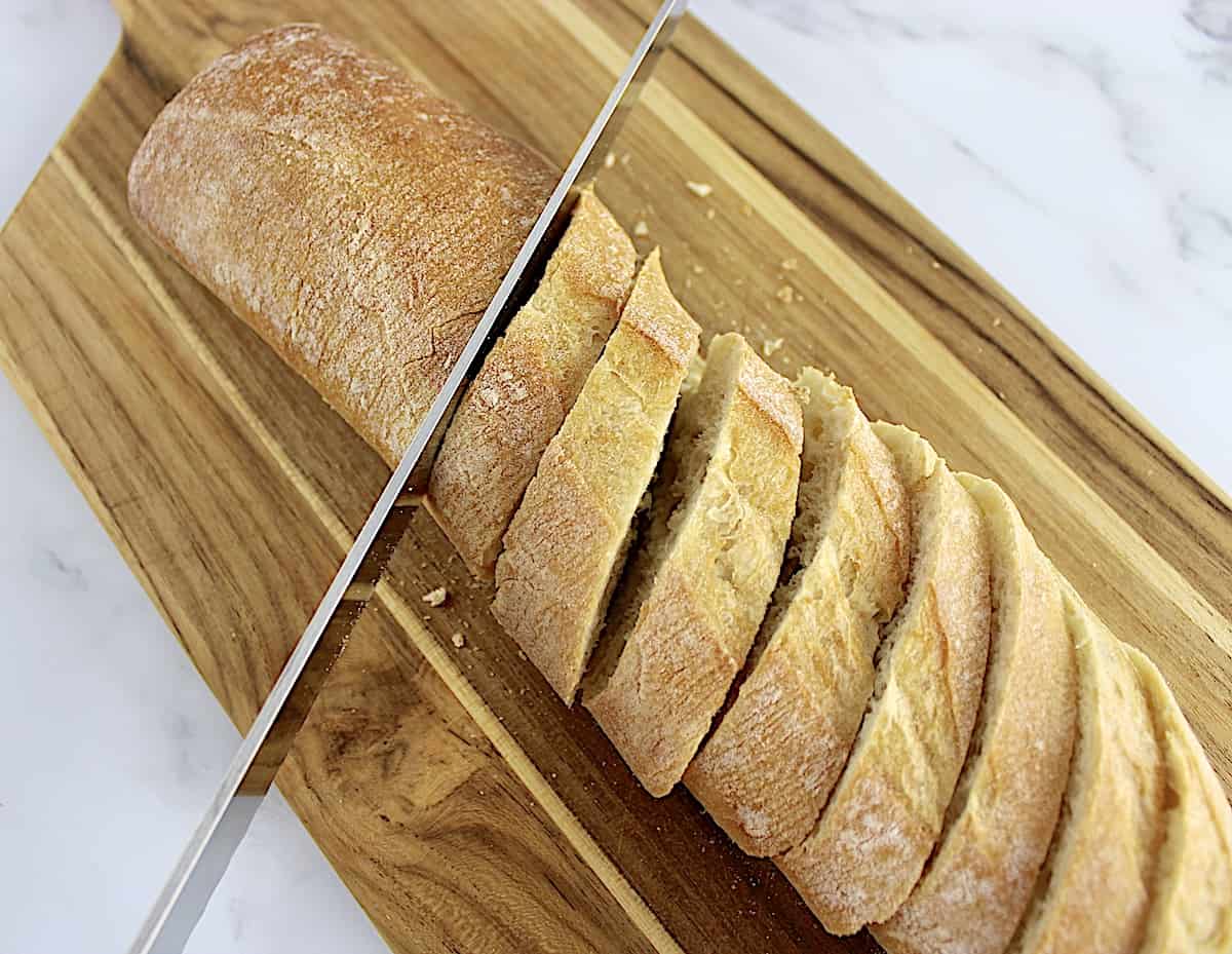 baguette being sliced on cutting board