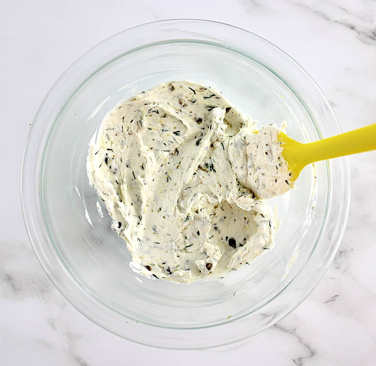 goat cheese spread for crostini in mixing bowl with yellow spoon
