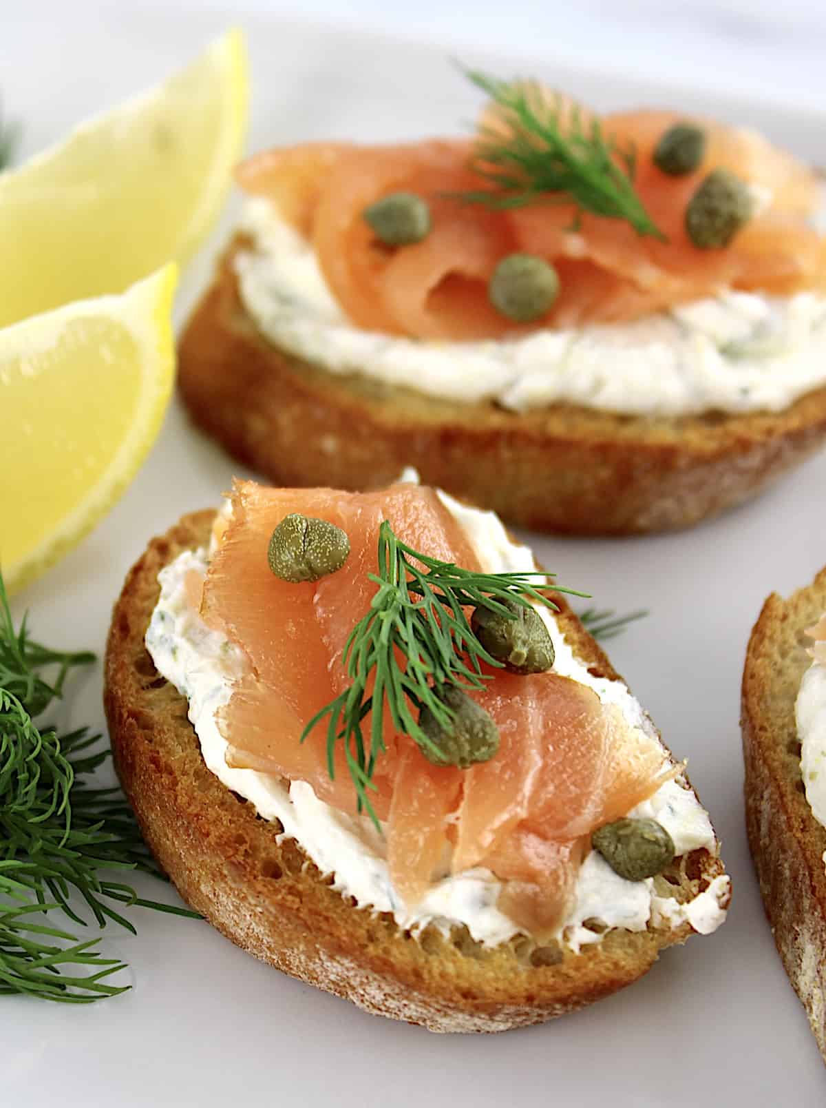 Smoked Salmon and Goat Cheese Crostini on white plate with dill and lemon wedges on side