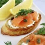Smoked Salmon and Goat Cheese Crostini on white plate with 2 lemon wedges