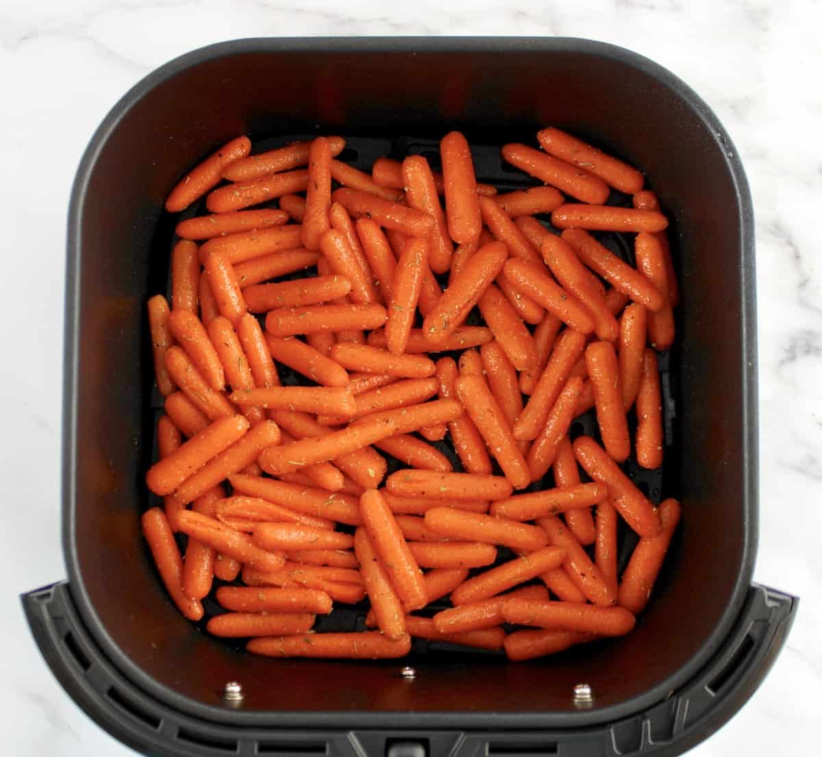 raw baby carrots with olive oil and spices in air fryer basket