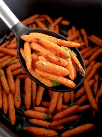 Air Fryer Baby Carrots in black serving spoon over air fryer basket