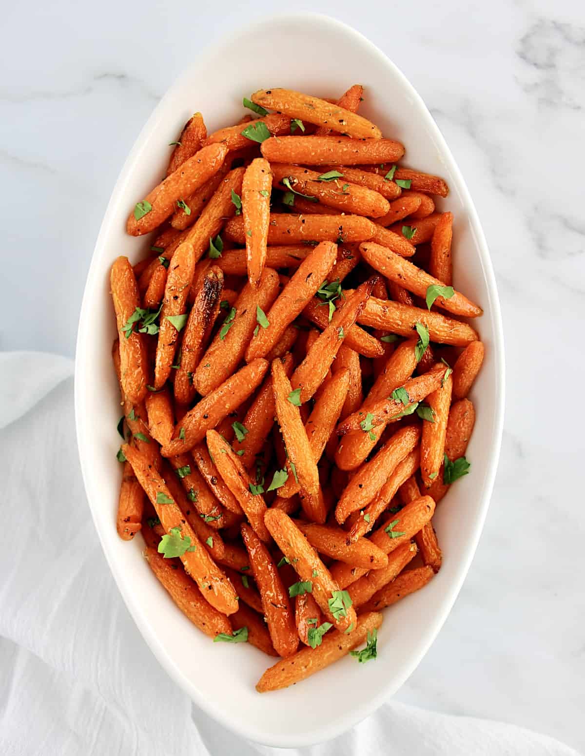 overhead view of Air Fryer Baby Carrots in white oval bowl with chopped parsley on top