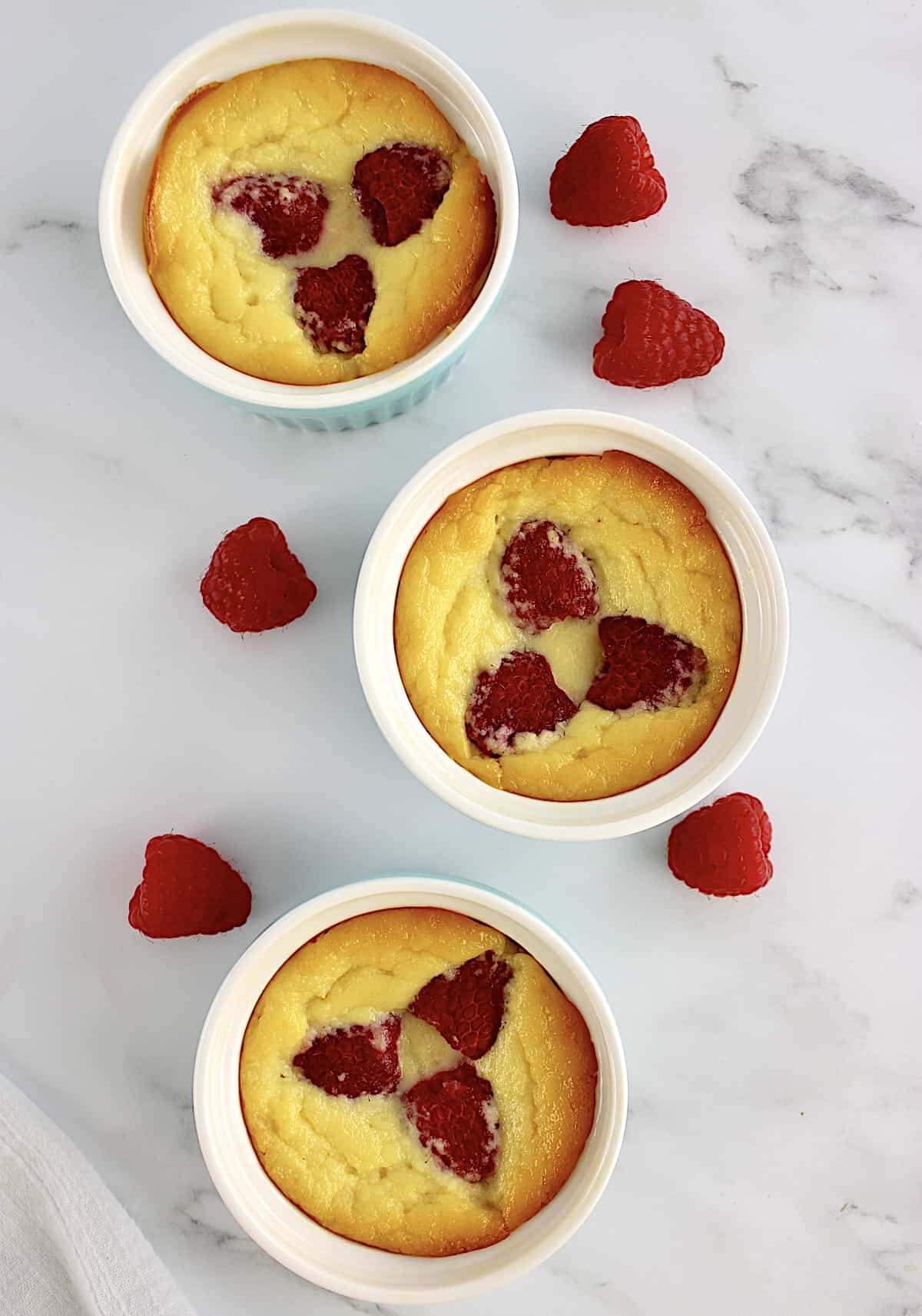 overhead view of 3 Baked Ricotta Raspberry Puddings with fresh raspberries on side