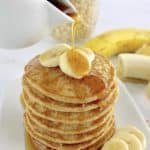 Banana Oat Flour Pancakes stack with sliced bananas on top and syrup being poured over top