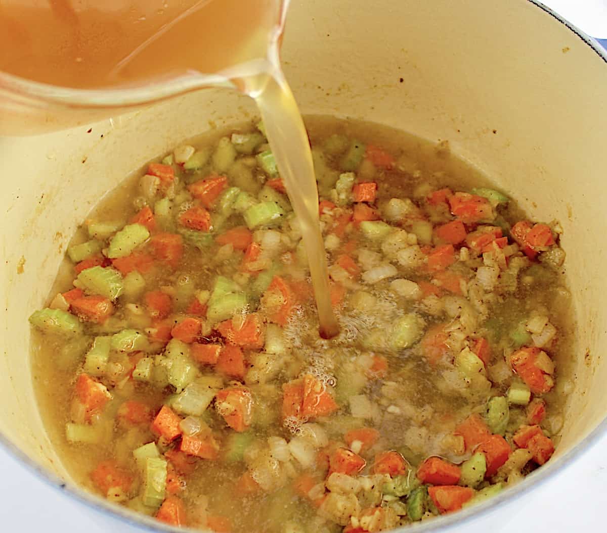 chicken broth being poured into pot with chopped veggies