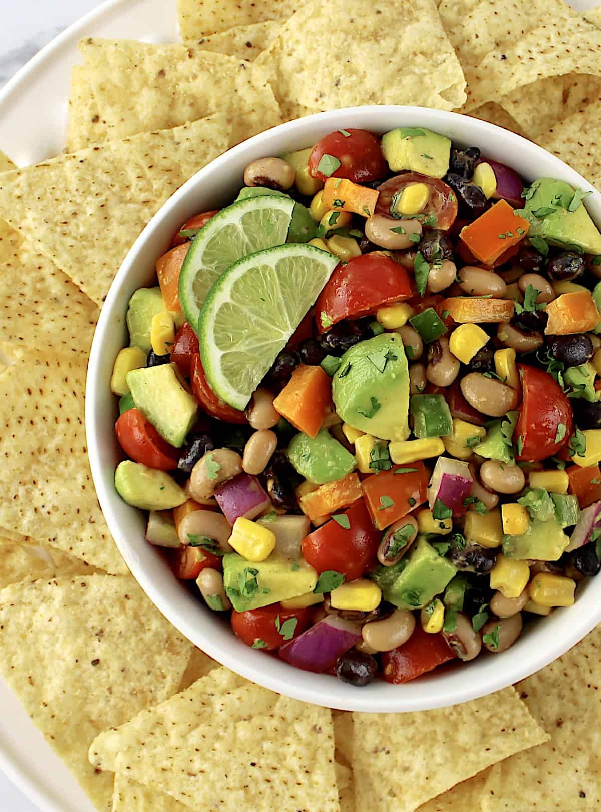 Cowboy Caviar in white bowl with 2 lime slices and tortilla chips around the bowl