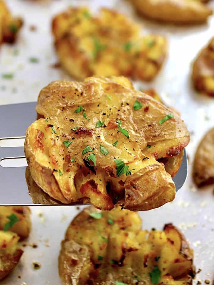 Crispy Smashed Potato on spatula held up over baking sheet