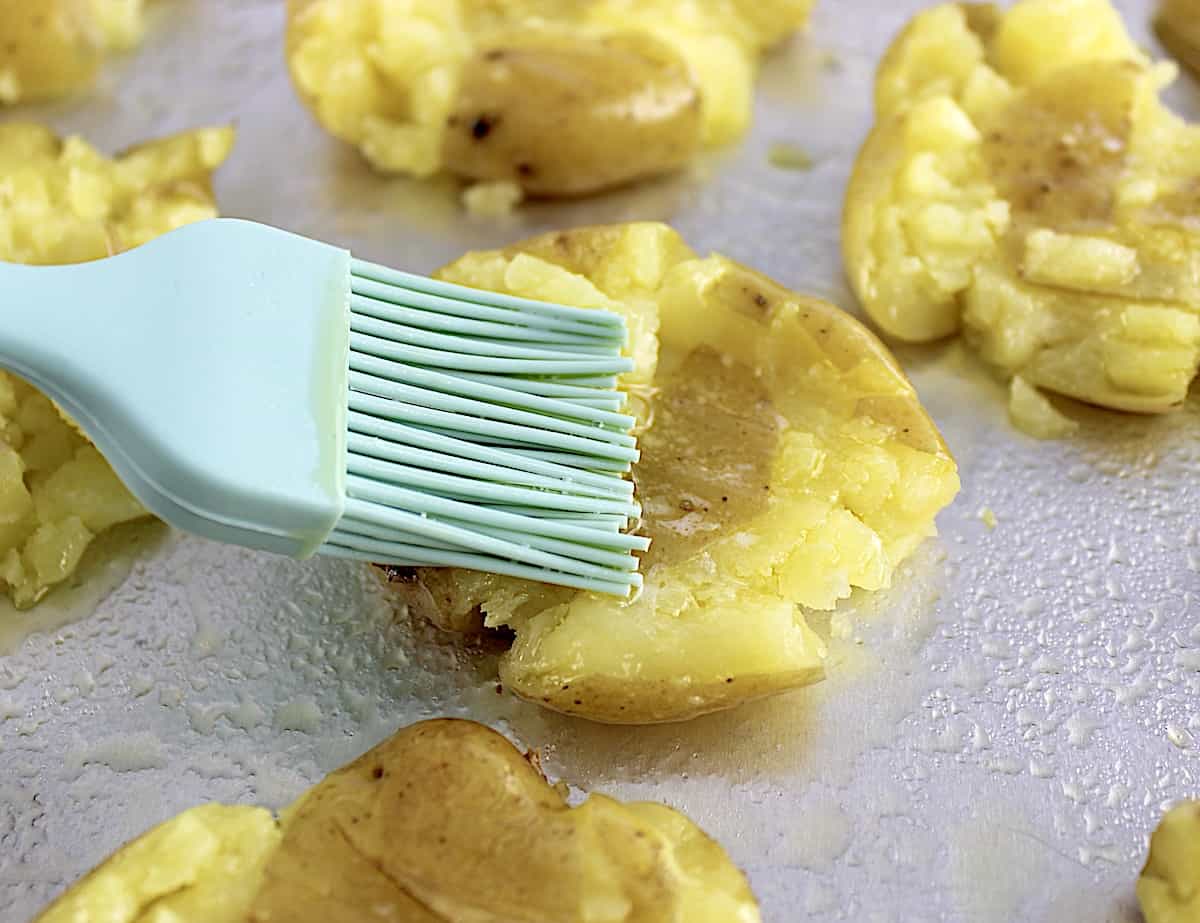 butter being brushed over smashed potato on baking sheet