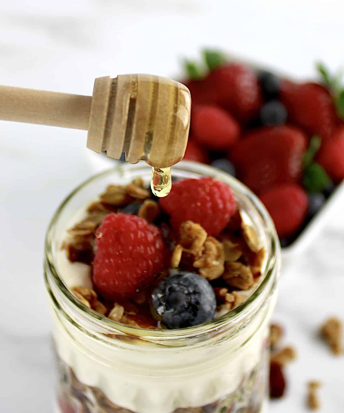 Easy Granola Parfaits with honey being drizzled on top with honey stick