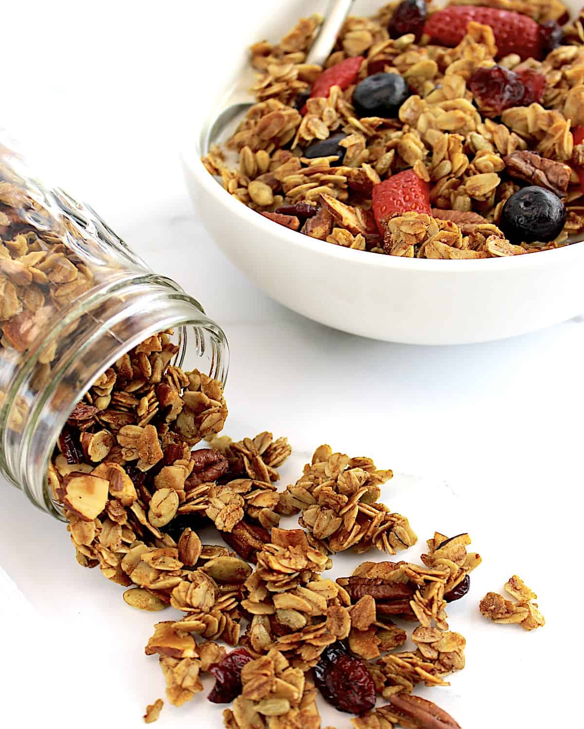 Homemade Granola spilling out of jar with cereal in bowl inn background