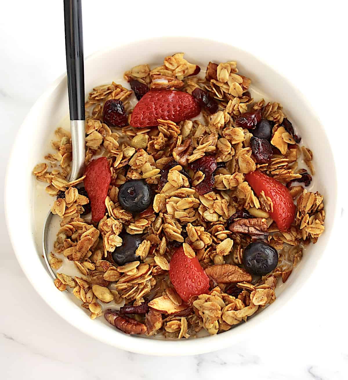 Homemade Granola cereal in white bowl with strawberries and blueberries