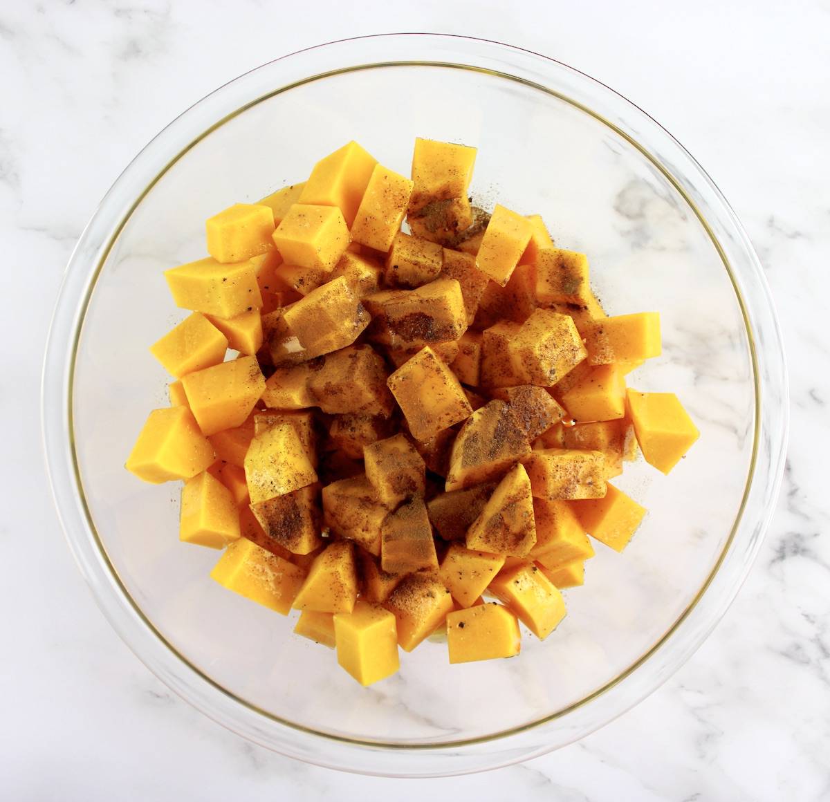 cubes of butternut squash in glass bowl with butter and cinnamon
