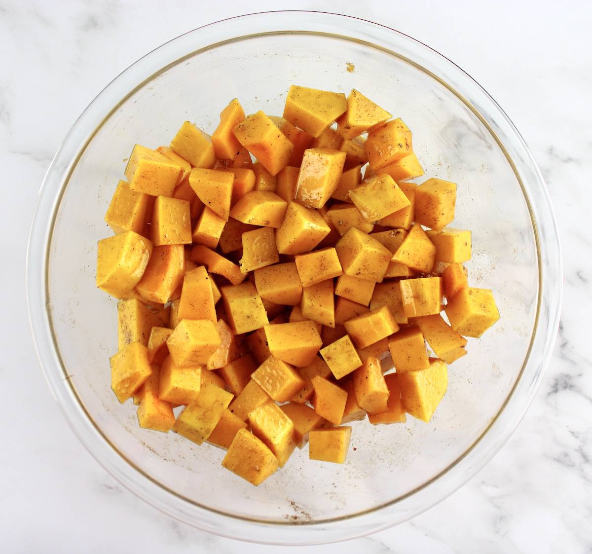 cubes of butternut squash in glass bowl with butter and cinnamon mixed