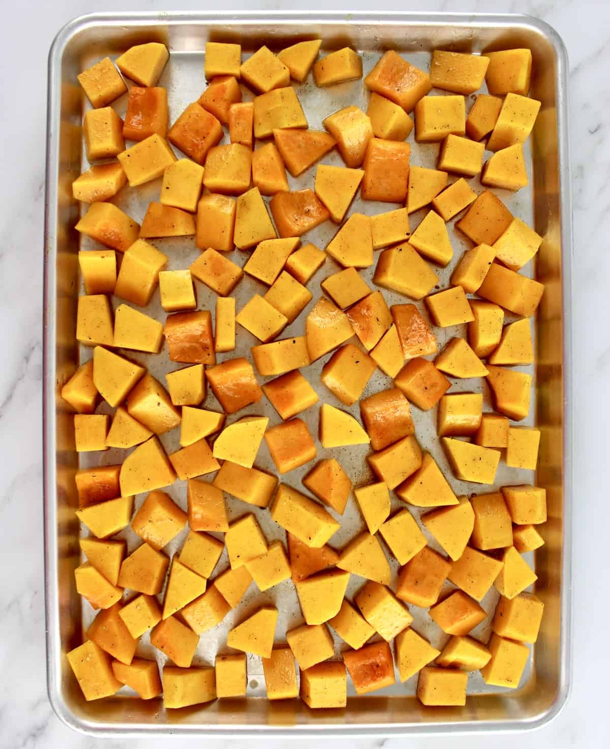 ucnooked butternut squash cubes on baking sheet with olive oil and cinnnamon