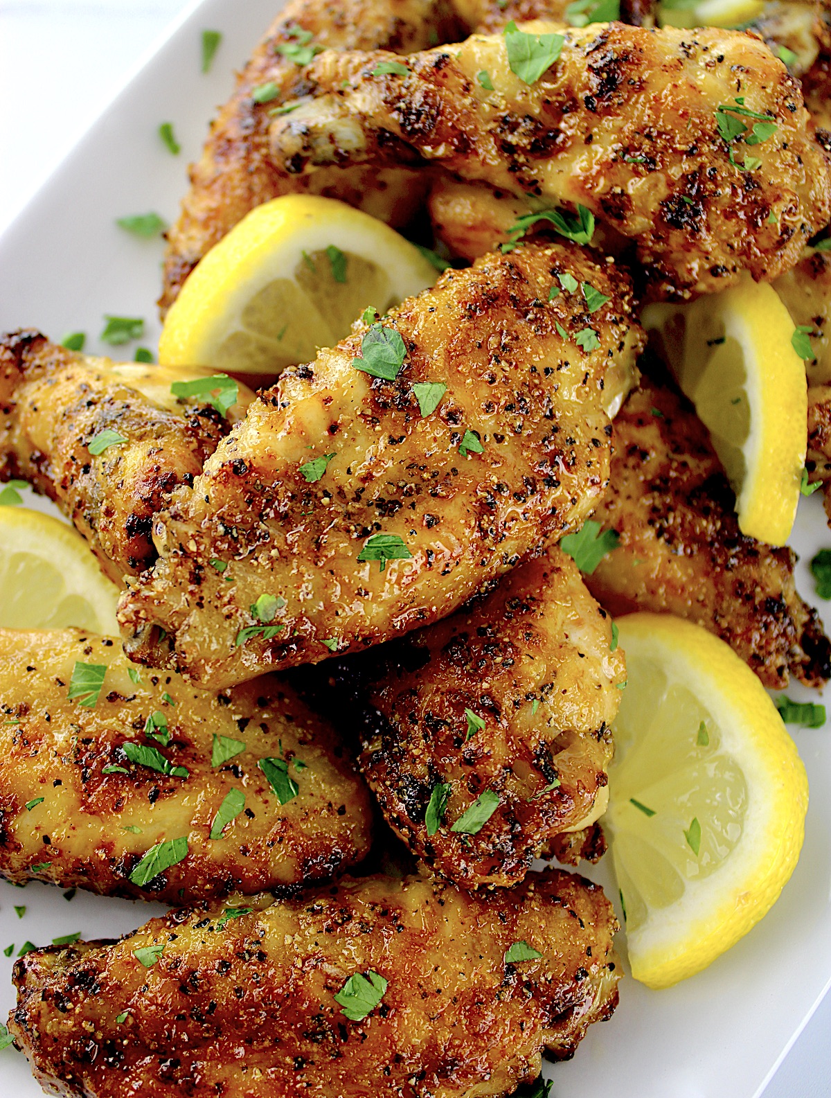 closeup of Lemon Pepper Chicken Wings on white plate with chopped parsley and lemon slices