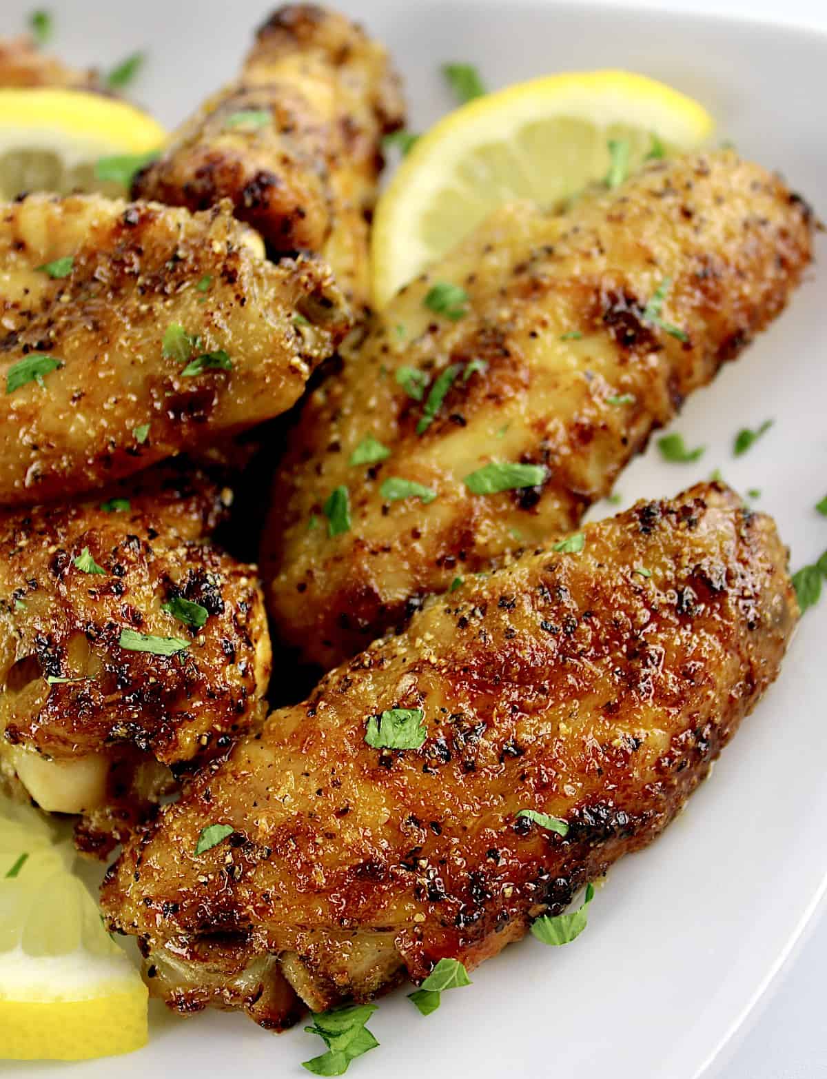 closeup of Lemon Pepper Chicken Wings on white plate with lemon slices