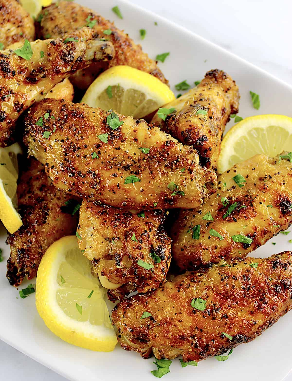 closeup of Lemon Pepper Chicken Wings on white plate with lemon slices
