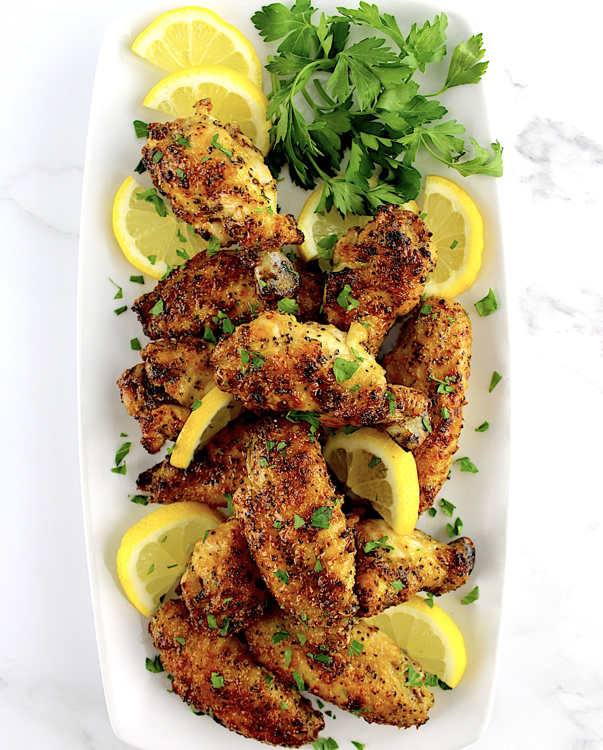 overhead view of Lemon Pepper Chicken Wings  on white platter with lemon slices and parsley garnish