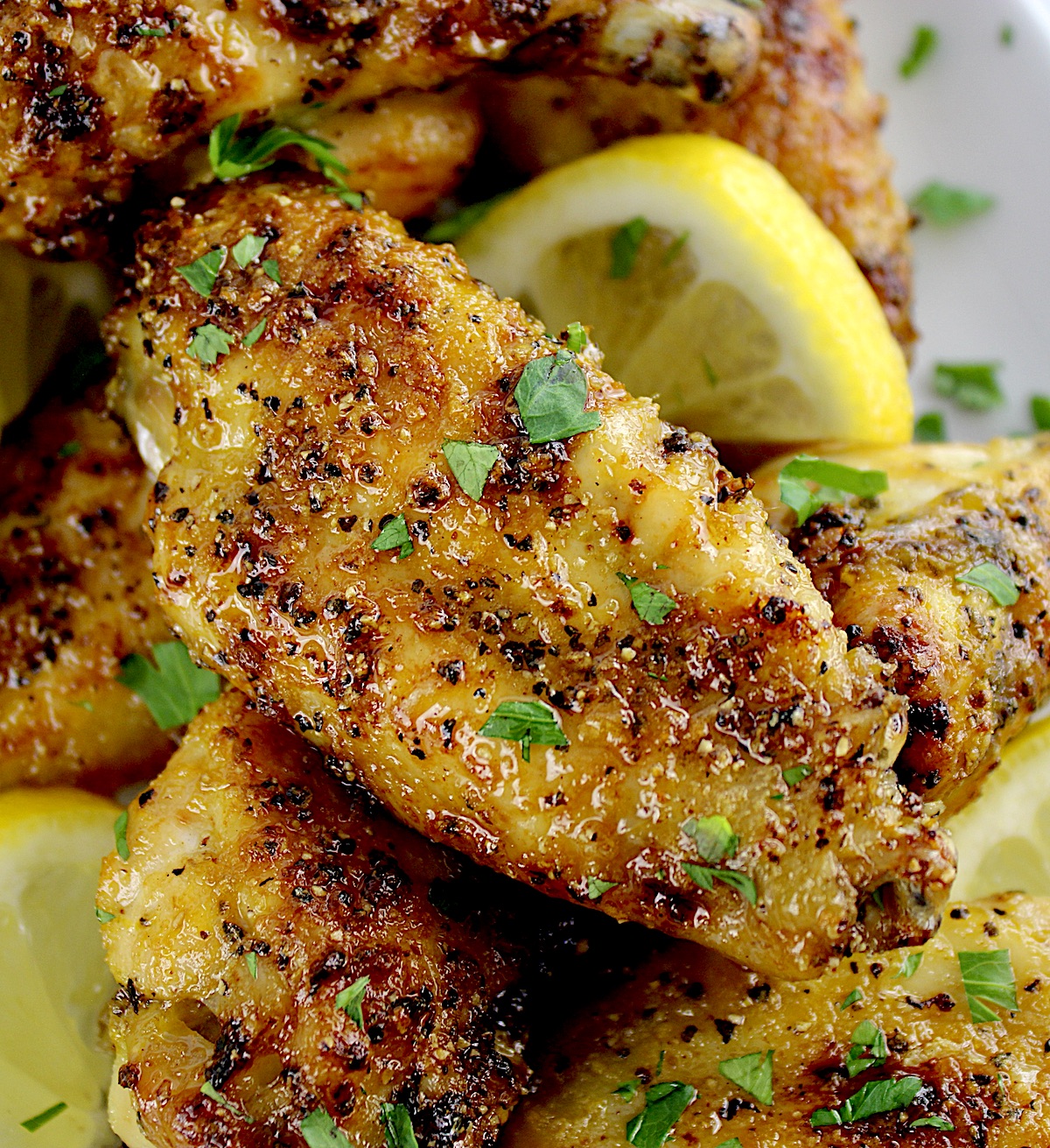 closeup of Lemon Pepper Chicken Wings on white plate with lemon slices