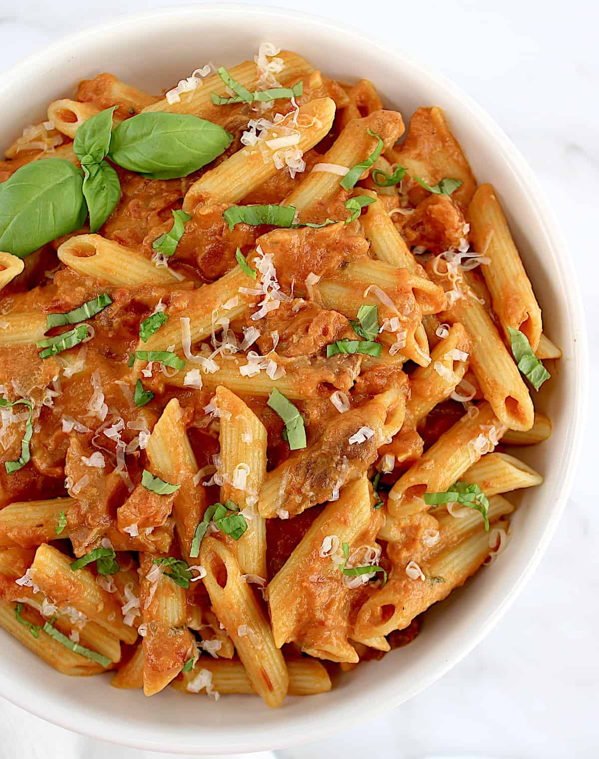 Penne Alla Vodka in white bowl with basil and parmesan cheese on top