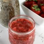 Strawberry Chia Seed Jam in open glass jar with strawberries and chia seeds in background
