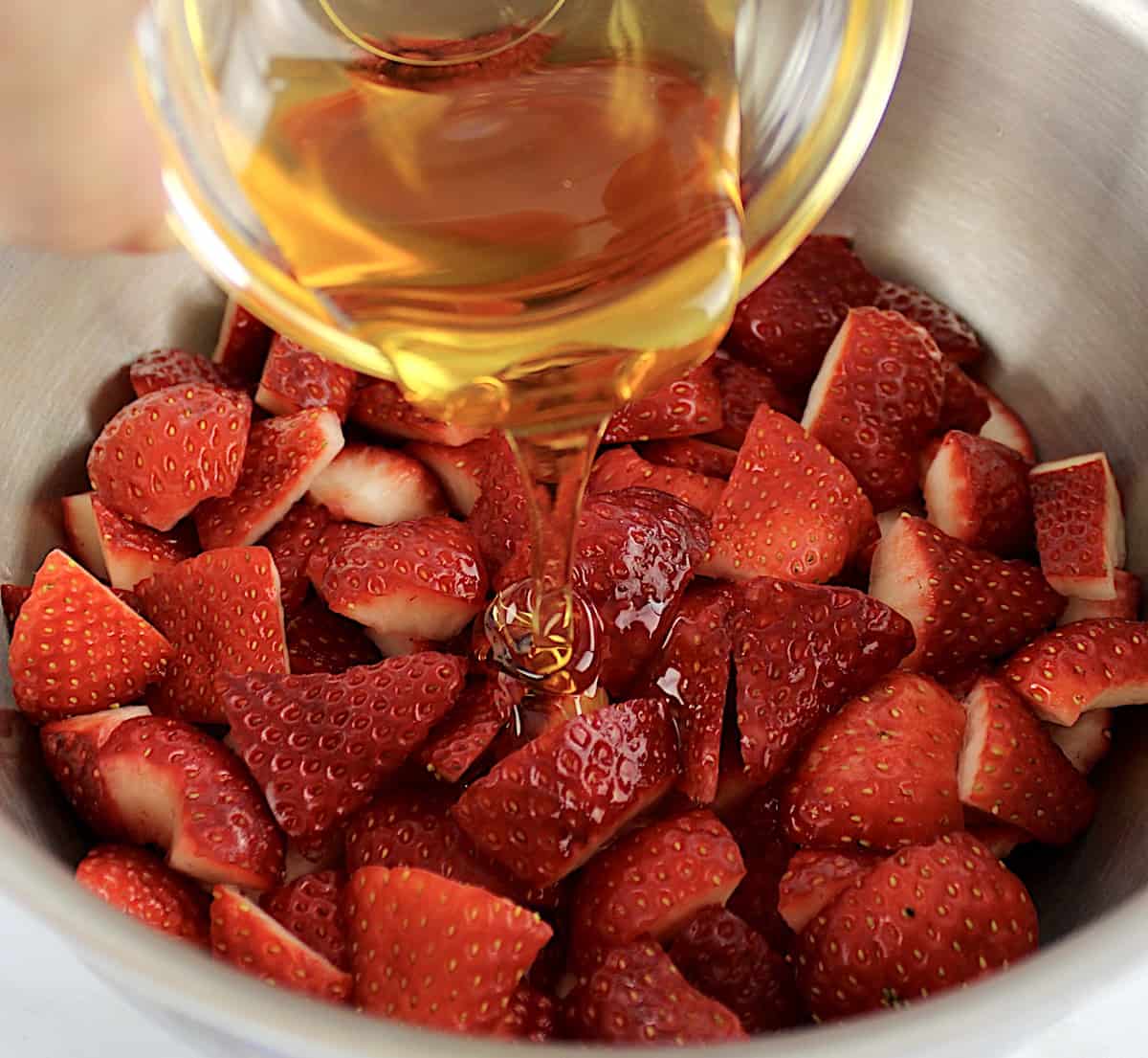 chopped strawberries in saucepan with honey being poured over