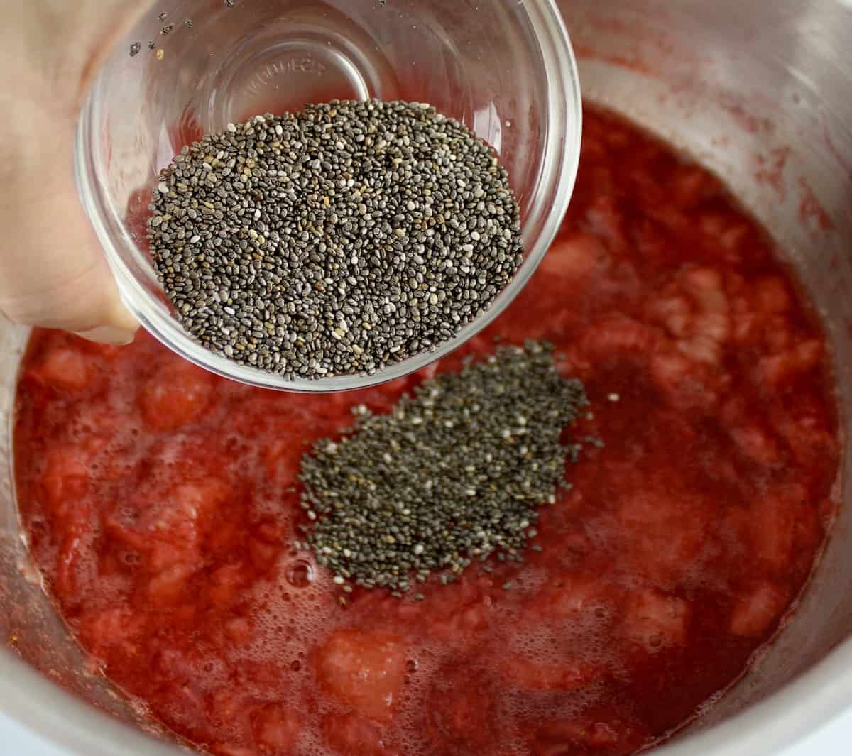 chia seeds being poured in cooked strawberries in saucepan