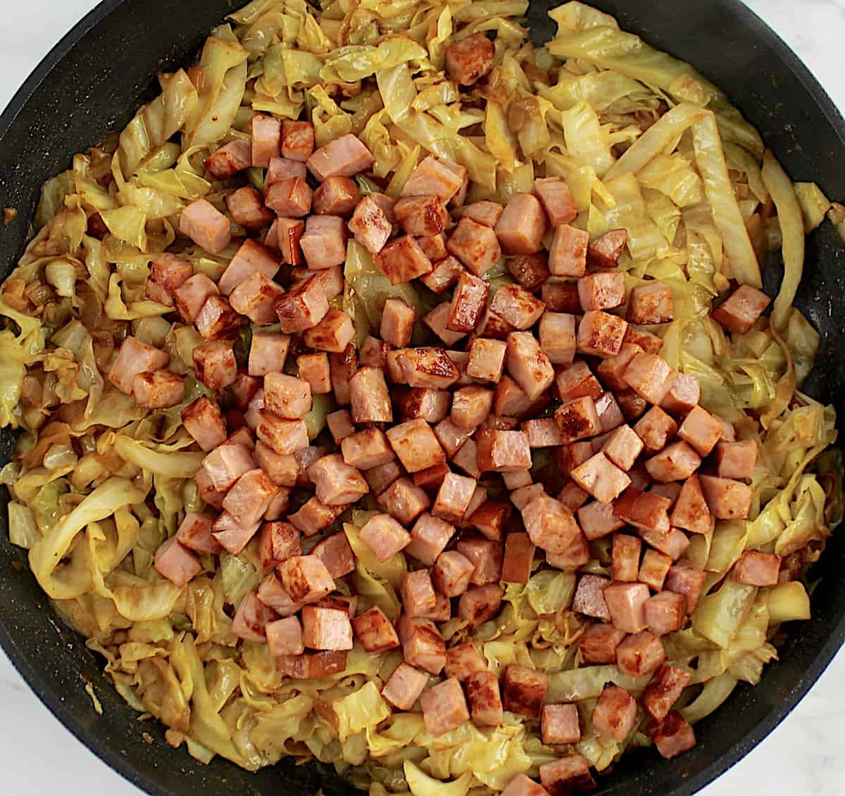 Fried Cabbage with Ham chunks on top in skillet